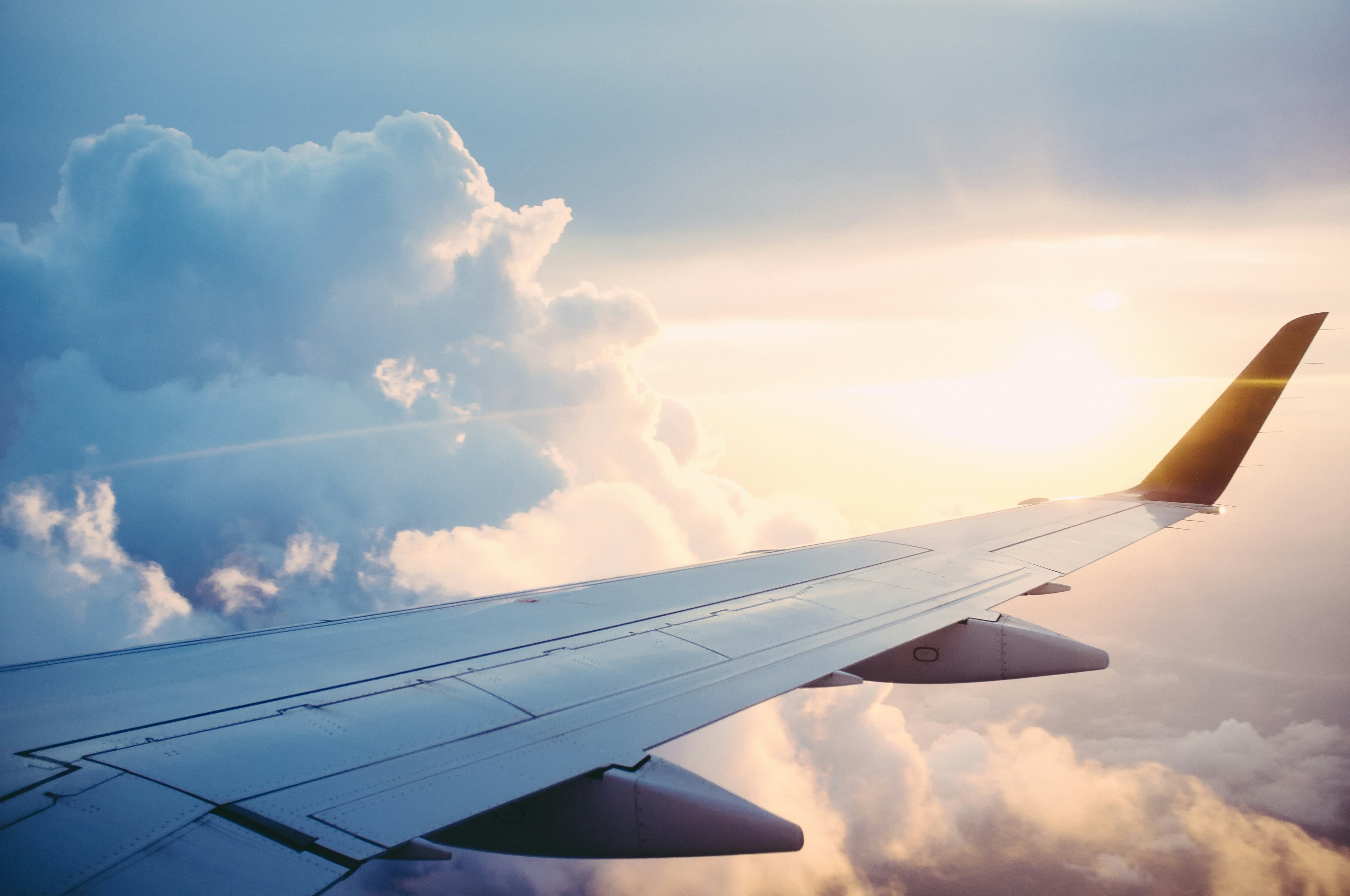 View of an airplane wing above the clouds through a cabin window